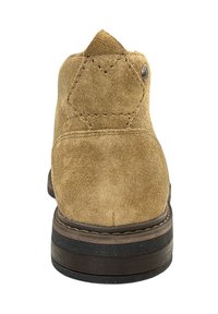 Stivale alla caviglia in suede beige con tacco appuntito, suola marrone a contrasto e dettagli di cucitura visibili. Presenta un accento metallico sul lato.