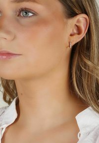 Silver hoop-örhänge med små klara kristaller, med en slät finish och en cirkulär design. Modellen har örat och en del av ansiktet synligt.