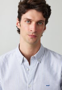 Chemise boutonnée à rayures verticales bleues et blanches, dotée d'un col, de boutons blancs et d'un petit logo bleu Levi's sur la poitrine.