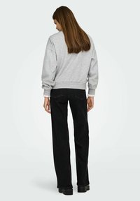 Hall halli pusa langevate õlgadega ja soonikkoes äärega, koos mustade kõrge vöökohaga teksadega. Komplekt on lõdvestunud lõike ja minimalistliku disainiga.