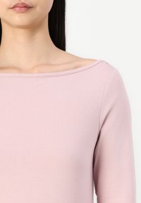 Lys rosa topp med off-shoulder design, lange ermer, laget av myk, glatt stoff, med en subtil ribbet halslinje.