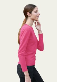 T-shirt à manches longues rose avec un col rond, en tissu doux et coupe slim, assorti à un jean foncé. Design simple et moderne.