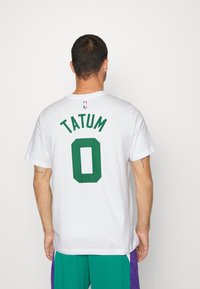 Hvid bomulds t-shirt med grøn "TATUM" tekst og nummeret "0" i et mesh-stil print på ryggen, NBA-logo ovenfor, korte ærmer.