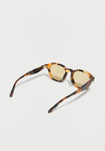 Lunettes de soleil à motif écaille de tortue avec montures arrondies et verres teintés brun clair reposant ouvertes sur une surface blanche.