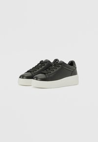 Baskets en cuir noir avec une texture lisse, semelle plateforme blanche et lacets noirs. Présente des clous décoratifs sur le côté.