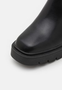 Czarne skórzane botki do kostki z okrągłym noskiem, grubą, teksturowaną podeszwą i gładką powierzchnią cholewki; minimalistyczny design bez widocznych elementów metalowych.