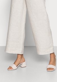 Białe plecione sandały na płaskiej podeszwie z masywnym obcasem, wykonane z materiału syntetycznego, z otwartym palcem i gładką teksturą.