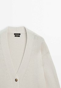 Cardigan en grosse maille écru avec un décolleté en V profond et une grande boutonnière unique à l'avant.