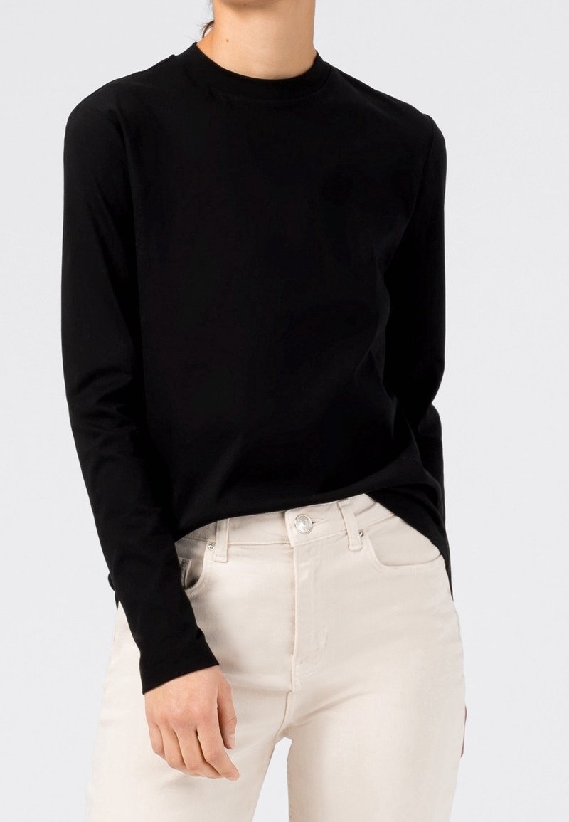 Mustapaita, jossa pitkät hihat ja pyöreä pääntie, tehty pehmeästä kankaasta. Yhdistetty vaalean beigeihin farkkuihin, joissa on napin ja vetoketjun yksityiskohta.