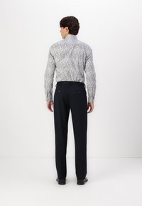 Cămașă cu butoni, cu un model floral albastru și alb, asortată cu pantaloni negri, ajustați. Cămășa are un guler înalt și mâneci lungi.
