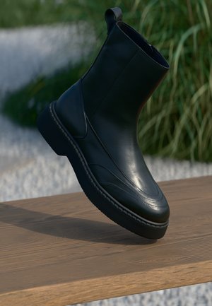 Botte cheville en cuir noir avec une texture lisse, bout rond et semelle contrastante. Comprend des détails de couture et une languette.
