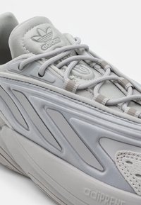 Harmaa urheilukenkä, jossa on teksturoitu pinta, sileät päällysteet ja kontrastivärit. Sisältää nauhoitusjärjestelmän ja pehmustetun pohjan.