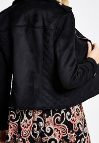 Giacca in eco-pelle scamosciata nera con texture trapuntata, hardware argentato e chiusura con zip, abbinata a una gonna con motivo paisley colorato.