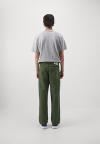 Gray cotton short-sleeve t-shirt paired with green cotton cargo pants featuring pockets. Model is seen from the back against a plain background.