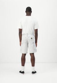 Light gray cargo shorts with multiple pockets, textured denim fabric, and a visible brand patch on the back. Paired with a plain white t-shirt.