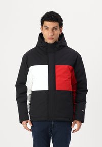 Veste rembourrée avec des blocs de couleur noirs, blancs et rouges. Design avec capuche et fermeture éclair, panneaux horizontaux et verticaux, et poignets élastiques.