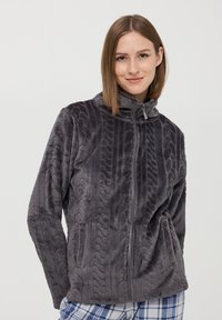 Giacca in pile grigia con un motivo a maglia a treccia testurizzata, colletto alto, zip frontale completa e tasche laterali. Tessuto morbido e vestibilità rilassata.
