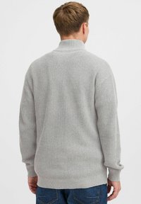 Suéter de punto gris claro con un cuello alto, textura acanalada y mangas largas. Presenta un corte relajado y un dobladillo recto en la cintura.