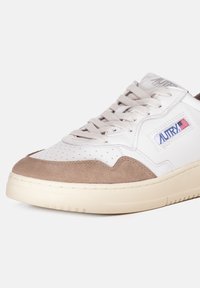 Zapatillas de ante blancas y marrones con puntera perforada, cierre con cordones en la parte frontal, media suela texturizada y parche de logo en el lado.