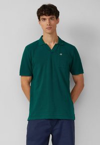 Grünes Poloshirt mit V-Ausschnitt, kurzen Ärmeln und einer Brusttasche mit kleinem Logo. Gewebte Textur, lässige Passform.