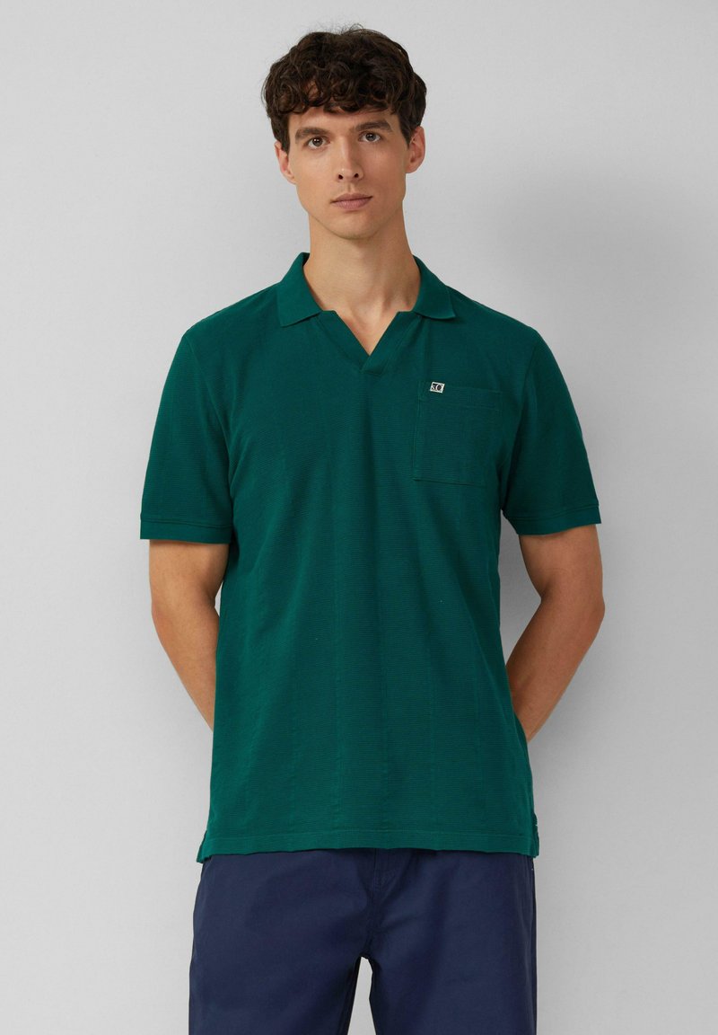 Grünes Poloshirt mit V-Ausschnitt, kurzen Ärmeln und einer Brusttasche mit kleinem Logo. Gewebte Textur, lässige Passform.