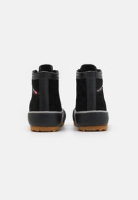 Botas de tornozelo pretas feitas de camurça com solas de borracha e uma sola de contraste castanha. Apresentam um acabamento texturizado e uma marcação mínima.