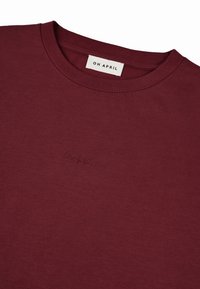 Bordo majica s okruglim izrezom, izrađena od mekog pamuka. Na prednjem dijelu se nalazi mali izvezeni logo "OH APRIL". Glatka tekstura.