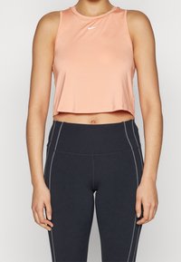 Persikofärgat kort atletiskt linne med rund halsringning och en liten vit Nike-logotyp, matchat med svarta leggings med gråa sidoseam.