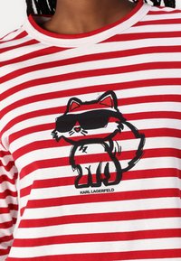 Chemise rayée rouge et blanche avec un renard de dessin animé portant des lunettes de soleil noires et le texte "KARL LAGERFELD" sous l'illustration.