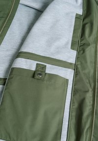 Grüner Oberstoff-Jacke mit einem hellgrauen Innenfutter. Verfügt über mehrere Taschen, darunter eine Tasche mit Druckknopfverschluss und kontrastierenden Texturen.