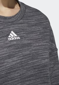 Sudadera gris melange con cuello redondo y mangas largas. Presenta un logo blanco de Adidas en el pecho y tejido texturizado.