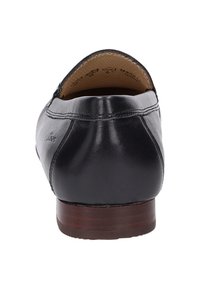 Mocassin en cuir noir avec un bout arrondi, des détails de couture et un petit talon en bois. Texture lisse avec une légère brillance.