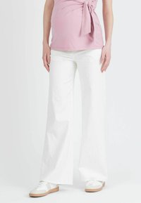 Pantalons blancs à jambes larges en tissu léger associés à des baskets blanches. Le tissu a une texture lisse et les pantalons présentent un design taille haute.