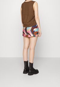 Haut marron sans manches à coupe décontractée, associé à une mini-jupe à motifs multicolores et des bottines noires à semelles épaisses.