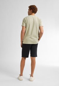 Camiseta de manga corta verde claro con cuello redondo, combinada con pantalones cortos negros. El conjunto presenta un corte holgado y un diseño sencillo.