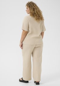 Beige twee-delig outfit gemaakt van lichtgewicht stof, met een losvallend top met korte mouwen en een wijde broek. Zwarte platform sandalen.
