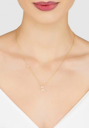 Gold necklace with a delicate chain featuring a shiny, stylized zodiac symbol and a small decorative bead accent.