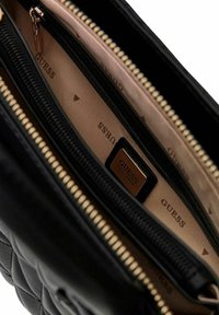 Borsa a tracolla nera trapuntata con più scomparti con cerniera, caratterizzata da un interno liscio con logo "GUESS" e dettagli in metallo color oro.