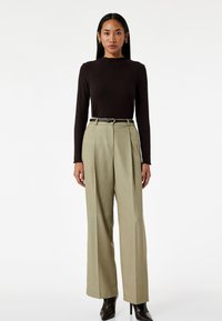 Bruine geribbelde lange mouw top gecombineerd met hooggenaaide, lichtgroene geplooide broek, accentueert met een zwarte riem en puntige zwarte hakken.