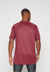 Camiseta deportiva color marrón hecho de una tela ligera y suave. Presenta mangas cortas, un escote redondo y costuras de la sisa tipo raglán.
