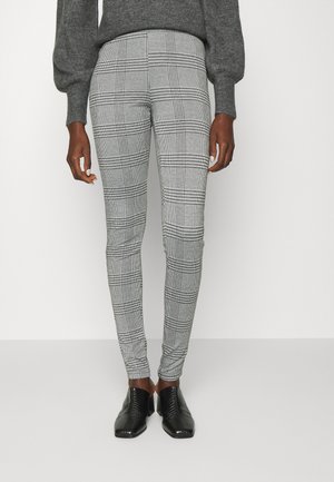 Leggings cinzentos com um padrão quadriculado, feitos de um tecido elástico. Combinados com sapatilhas pretas texturizadas.