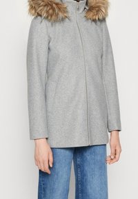 Abrigo de lana gris con capucha forrada de piel, cierre de cremallera y bolsillos laterales. Mangas de corte recto y textura suave.