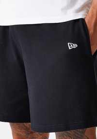 Bermuda nera in tessuto strutturato, con un logo bianco sul lato sinistro. Il capo ha una vestibilità comoda e orlo cucito.