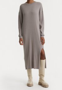 Abito a maniche lunghe a costine di colore grigio chiaro, con uno spacco laterale e una vestibilità comoda. Abbinato a stivali beige fino al ginocchio.
