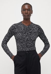 Haut noir à manches longues avec un motif abstrait blanc, en tissu texturé avec des détails froncés à l'avant, associé à un pantalon noir sur mesure.