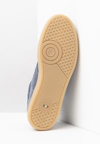 Suela de zapato de goma marrón con un patrón texturizado, que presenta un diseño circular en el centro y un logo grabado en el talón.