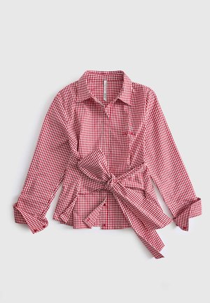 Chemise à manches longues en vichy rouge et blanc avec un col et un grand nœud noué à la taille, manches retroussées aux poignets, posée à plat sur fond blanc.