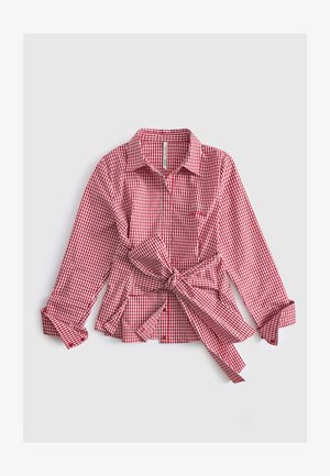 Chemise à manches longues en vichy rouge et blanc avec un col et un grand nœud noué à la taille, manches retroussées aux poignets, posée à plat sur fond blanc.