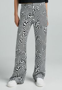 Svartvit mönstrade byxor med en vågig design och blommiga detaljer, tillverkade av ett mjukt tyg, kombinerat med vita sneakers.