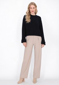 Marineblå cropped sweater med lange ærmer, parret med beige vide bukser. Glatte stoffers teksturer og minimalistiske designede detaljer.